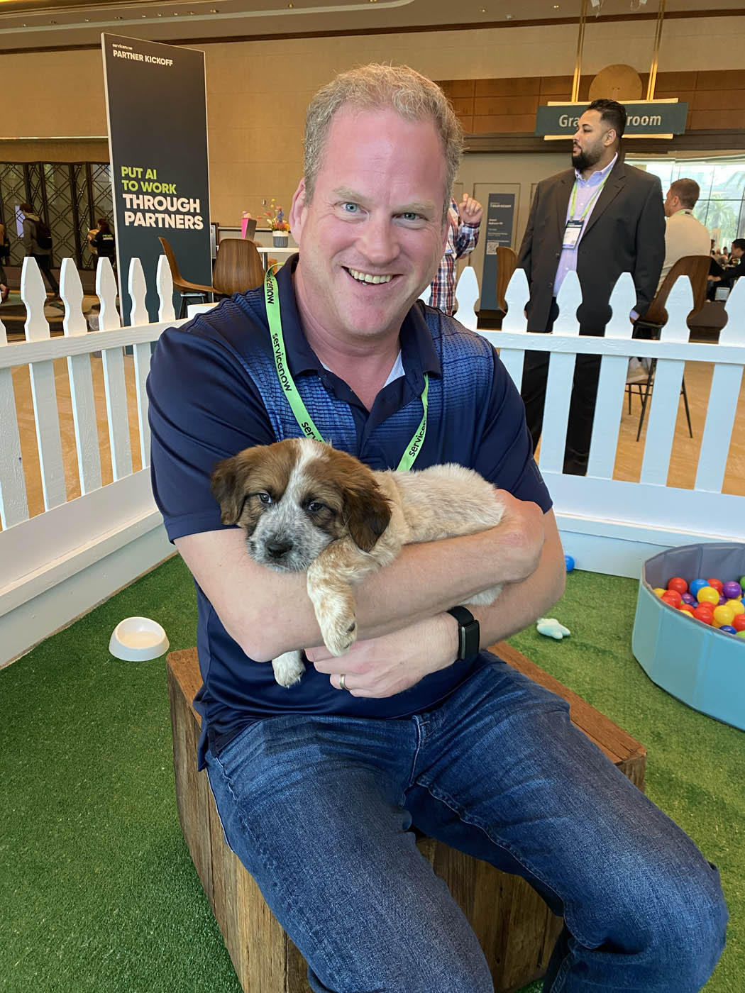 A man in a blue shirt holding a puppy and sitting down on a chair at their event with Puppy Love in Silicon Valley / Bay Area.
