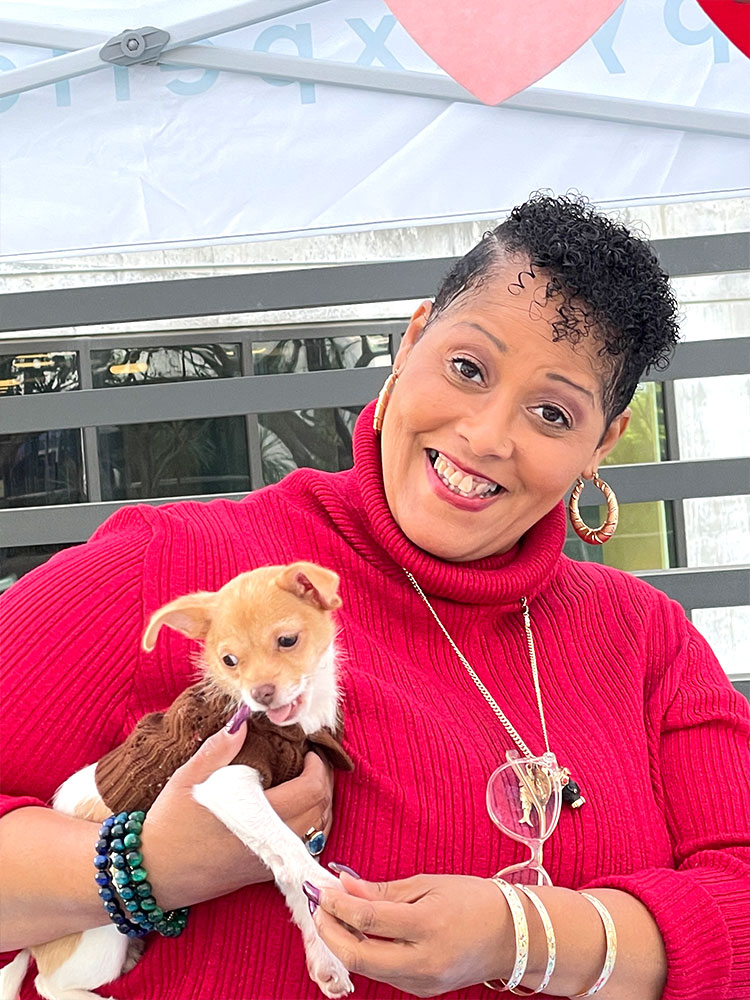 A woman in a red shirt holding a puppy at a lincoln property company Puppy Love™ Southern California event.