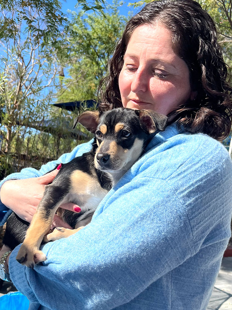 A woman in a blue shirt holding a puppy and smiling - feeling the benefits of adding Puppy Love to their Silicon Valley / Bay Area company wellness programs.