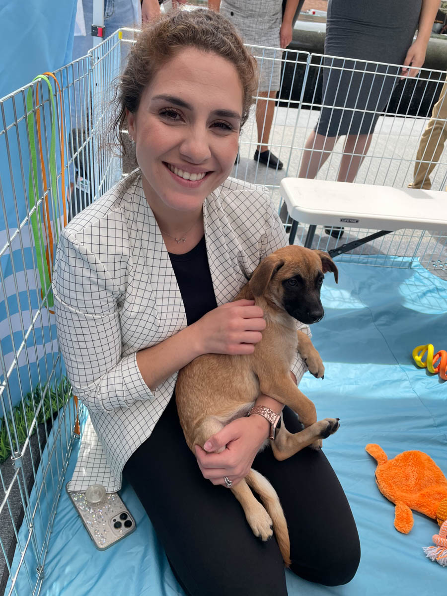 A woman holding in a white shirt holding an adorable puppy while sitting at a Puppy Love™ event for commonwealth.