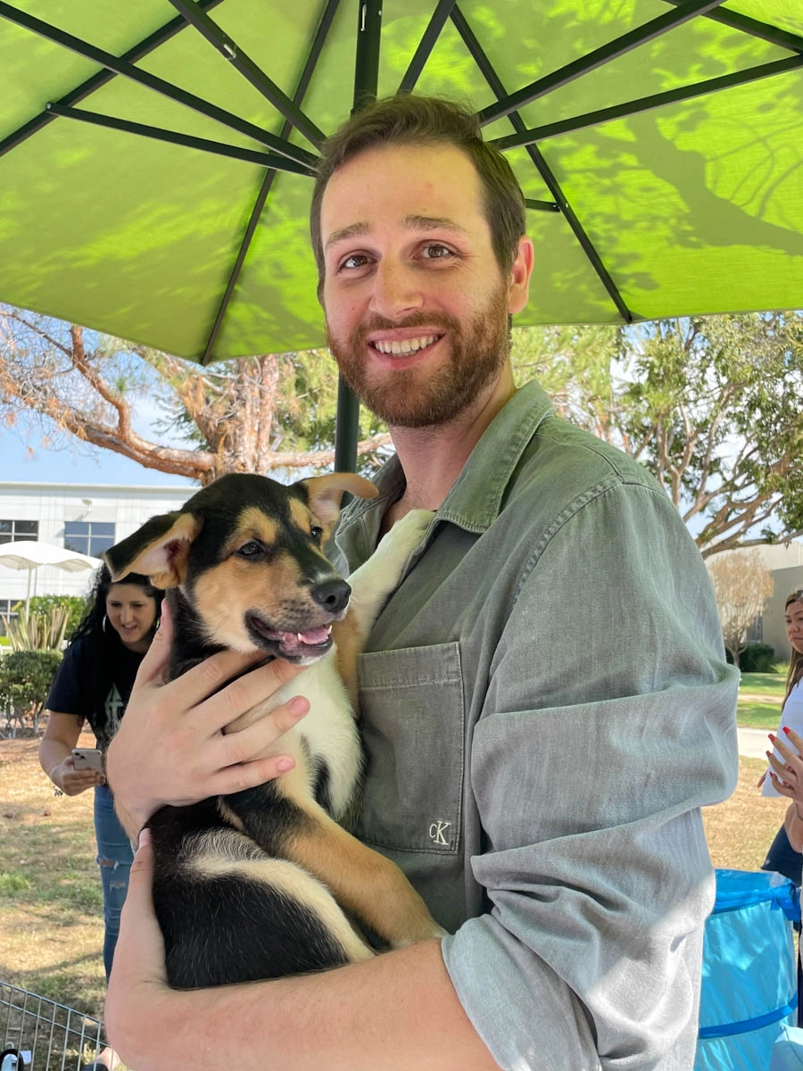 A man under a green umbrella standing out side with a Puppy Love™ puppy.