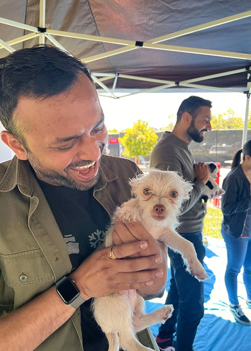 A tesla employee laughing and holding a puppy at puppy love's puppy lounge during the tesla appreciation event.
