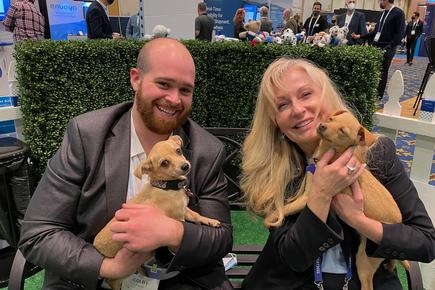 Puppies At A Trade Show? Genius!! 3 Man and women holding two golden pups.